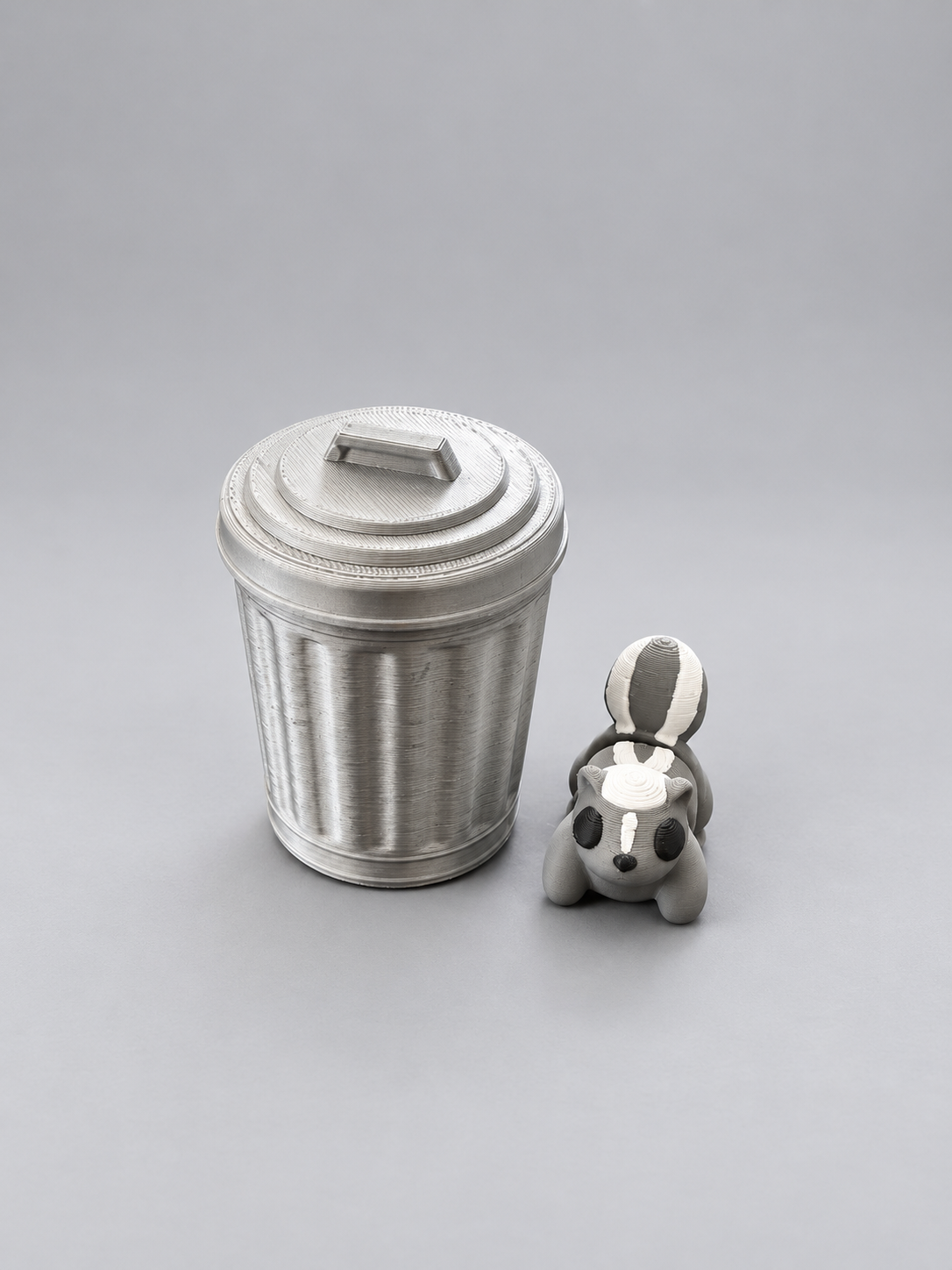 Articulated grey, white and black skunk beside its silver bin with twist-and-lock lid